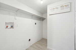 Laundry area with a textured ceiling, hookup for an electric dryer, wood finish floors, laundry area, and washer hookup