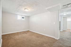 Below grade area with baseboards, carpet flooring, a textured ceiling, and visible vents