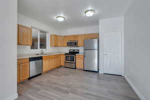 Kitchen featuring light wood finished floors, light countertops, a sink, baseboards, and appliances with stainless steel finishes
