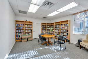 Community library with wall of books, a paneled ceiling, visible vents, and a healthy amount of sunlight