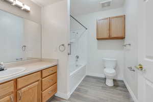 Bathroom with wood finished floors, visible vents, shower / bath combination, toilet, and vanity