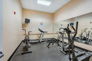 Clubhouse Exercise room featuring a drop ceiling and baseboards