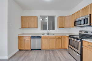 Kitchen with appliances with stainless steel finishes, a sink, light countertops, and light wood-style floors