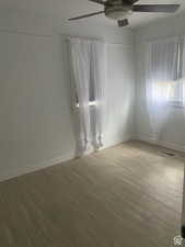 Empty room featuring wood finished floors, visible vents, baseboards, and ceiling fan