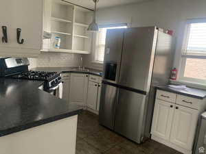 Kitchen featuring dark countertops, a sink, stainless steel appliances, white cabinets, and backsplash