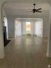 Unfurnished living room featuring a ceiling fan, wood finished floors, and arched walkways