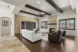 Living area with a barn door, a ceiling fan, a large fireplace, baseboards, and beam ceiling