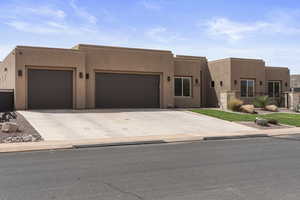 Pueblo-style home featuring a garage, concrete driveway, stucco siding, and fence