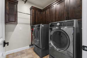 Clothes washing area featuring separate washer and dryer, baseboards, cabinet space, and stone tile floors