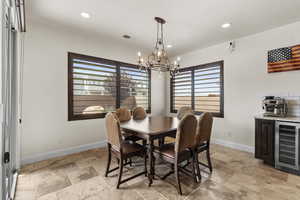 Dining space with beverage cooler, stone tile floors, a notable chandelier, and visible vents