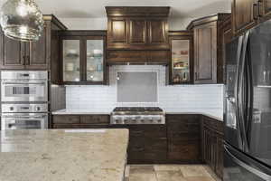 Kitchen featuring dark brown cabinets, light stone countertops, and appliances with stainless steel finishes