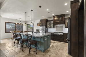 Kitchen featuring backsplash, stone tile flooring, a kitchen breakfast bar, and appliances with stainless steel finishes