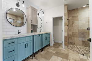 Full bath featuring toilet, a sink, double vanity, and a tile shower