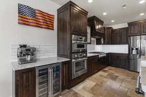 Kitchen featuring dark brown cabinets, beverage cooler, stainless steel appliances, backsplash, and visible vents