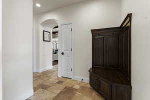 Hall with stone tile flooring, baseboards, arched walkways, and recessed lighting