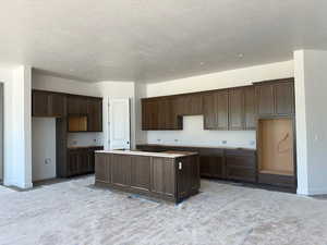 Kitchen with a center island, dark brown cabinets, baseboards, and a textured ceiling