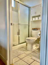 Bathroom with toilet, a shower stall, tile patterned flooring, and baseboards