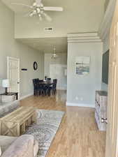 Living area featuring ceiling fan, a high ceiling, light wood-type flooring, and baseboards