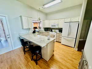 Kitchen featuring white appliances, a peninsula, a sink, a breakfast bar, and white cabinets