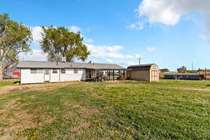 Back of house with a storage unit, fence, a lawn, an outdoor structure, and a patio