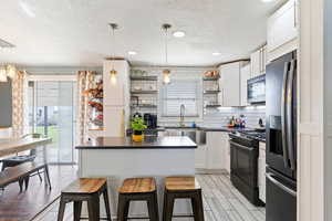 Kitchen featuring dark countertops, open shelves, a sink, a textured ceiling, and appliances with stainless steel finishes