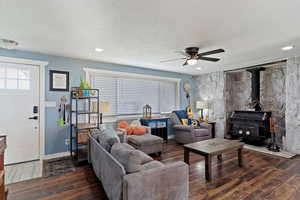 Living room featuring a ceiling fan, a wood stove, wood finished floors, and a textured ceiling