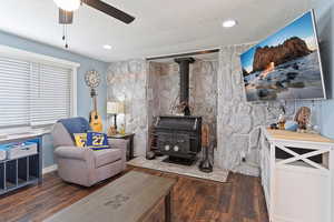 Living area featuring a wood stove, wood finished floors, a textured ceiling, and a ceiling fan