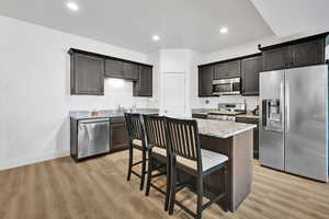 Kitchen with light stone counters, light wood-type flooring, a kitchen bar, baseboards, and appliances with stainless steel finishes
