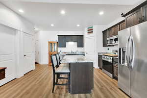 Kitchen with light stone counters, appliances with stainless steel finishes, light wood-style floors, and a kitchen island