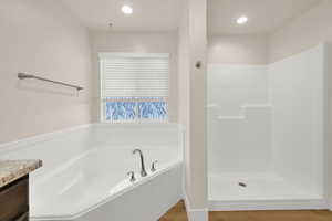 Full bathroom with recessed lighting, walk in shower, a garden tub, vanity, and wood finished floors