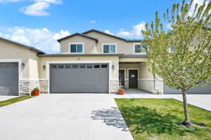 View of front of home featuring a garage, driveway, stone siding, and stucco siding