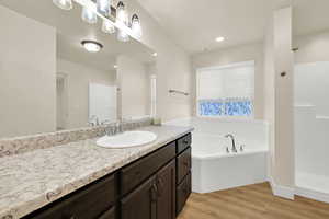 Bathroom featuring a garden tub, wood finished floors, walk in shower, vanity, and recessed lighting