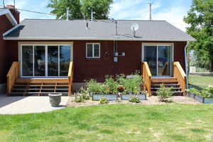Rear view of property featuring a lawn, a garden, entry steps, and roof with shingles