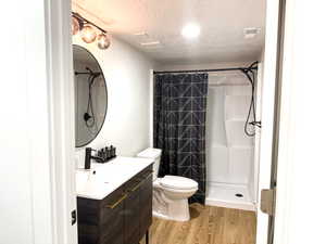 Bathroom with wood finished floors, visible vents, vanity, walk in shower, and a textured ceiling