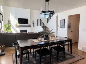 Dining area featuring stairway, wood finished floors, a fireplace, a notable chandelier, and visible vents