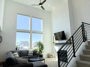 Living room featuring stairs, a ceiling fan, carpet flooring, and a towering ceiling