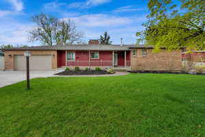 Ranch-style house with concrete driveway, a chimney, covered porch, an attached garage, and a front yard