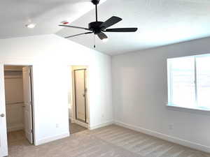 Unfurnished bedroom featuring a spacious closet, vaulted ceiling, and multiple windows