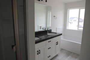 Bathroom featuring a garden tub, wood finished floors, a sink, and double vanity