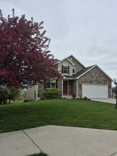 Traditional home featuring stone siding, an attached garage, a front yard with blossoming trees, and concrete driveway