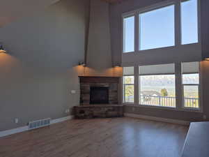 Unfurnished living room with wood finished floors, baseboards, high vaulted ceiling, and a stone fireplace
