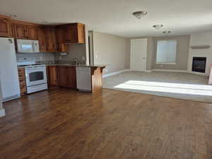 Kitchen with dark wood-style floors, stone countertops, a sink, white appliances, and open floor plan