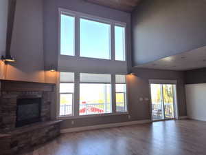 Unfurnished living room featuring wood finished floors, baseboards, a stone fireplace, and a towering ceiling