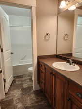 Divided full bathroom featuring bathtub / shower combination, vanity, stone finish flooring, and toilet