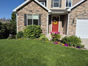 Property entrance with stone siding, flowers currently blooming and a lawn