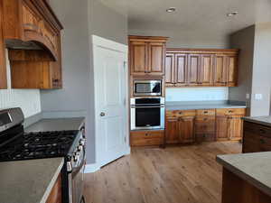 Kitchen featuring cherry cabinetry, appliances with stainless steel finishes, two ovens, and light hardwood flooring
