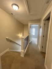 Corridor featuring an upstairs landing, attic access, visible vents, and carpet floors