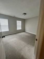 Carpeted spare room featuring a textured ceiling, visible vents, and baseboards