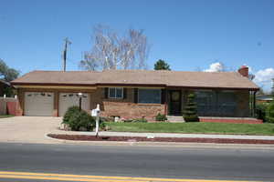 Single story home featuring a tile roof, brick siding, an attached garage, and a front lawn