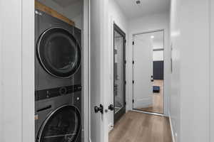 Laundry area featuring light wood-type flooring, visible vents, and stacked washing maching and dryer